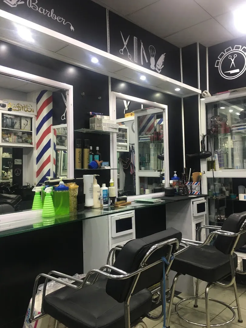 Inside Hair Care Barber Shop: chrome-and-black barber chairs along a glass-topped counter, with matte black walls carrying white line-art icons of scissors, comb, razor, and the Hair Care wordmark